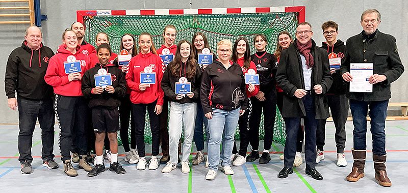 Gruppe von Sportlerinnen mit Urkunden in Sportkleidung vor einem Handballtor.